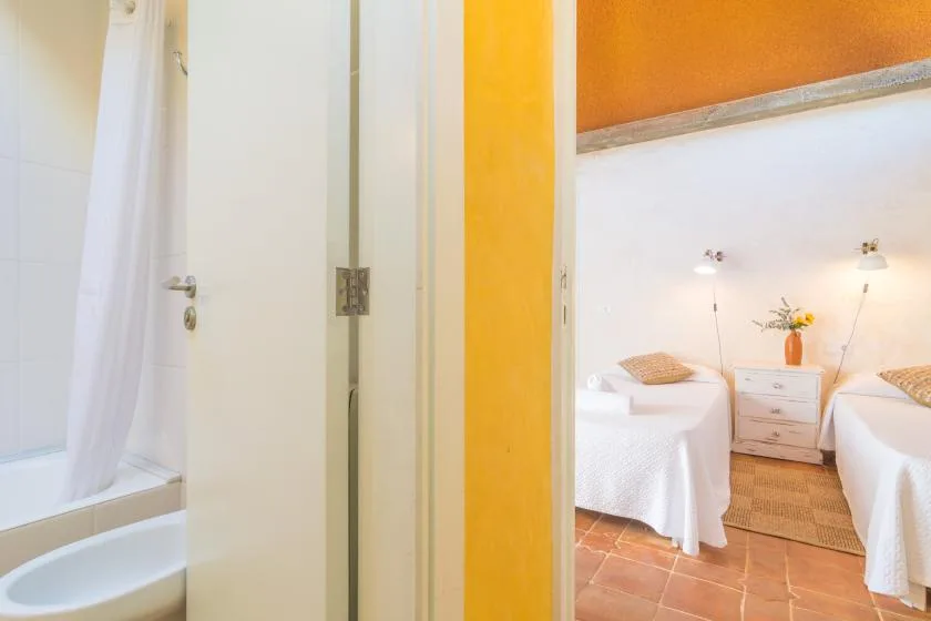 Un dormitorio luminoso con dos camas, una mesita de noche y un baño contiguo.