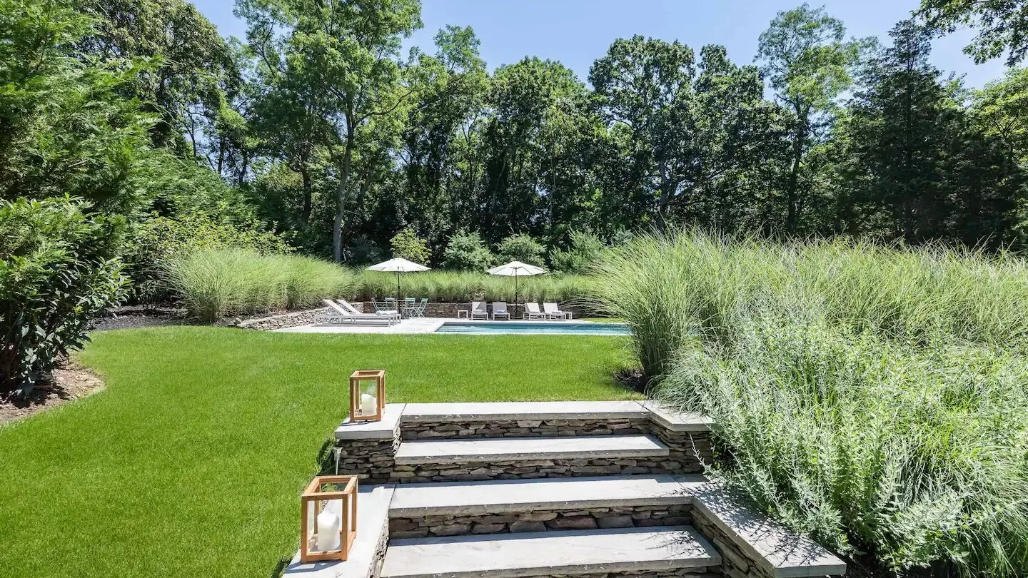 Un jardín cuidado conduce a una piscina exterior más allá de unos escalones de piedra.