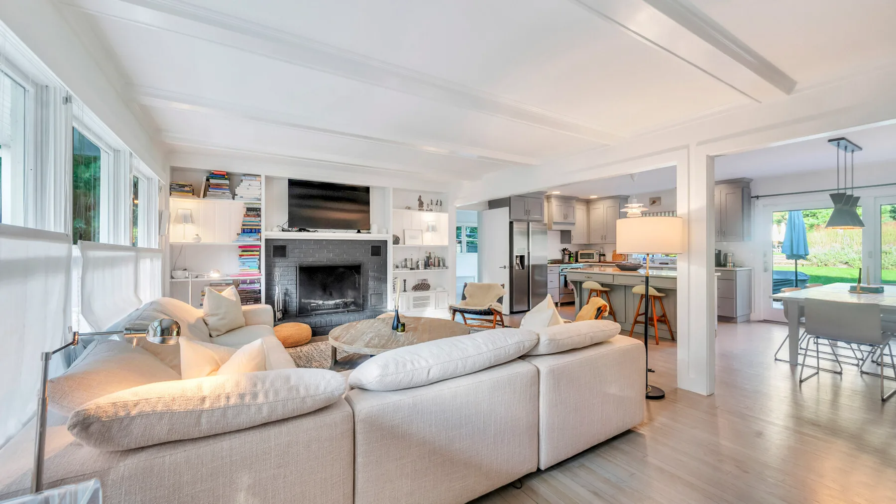 Una luminosa sala de estar diáfana con asientos blancos y una chimenea junto a la cocina.