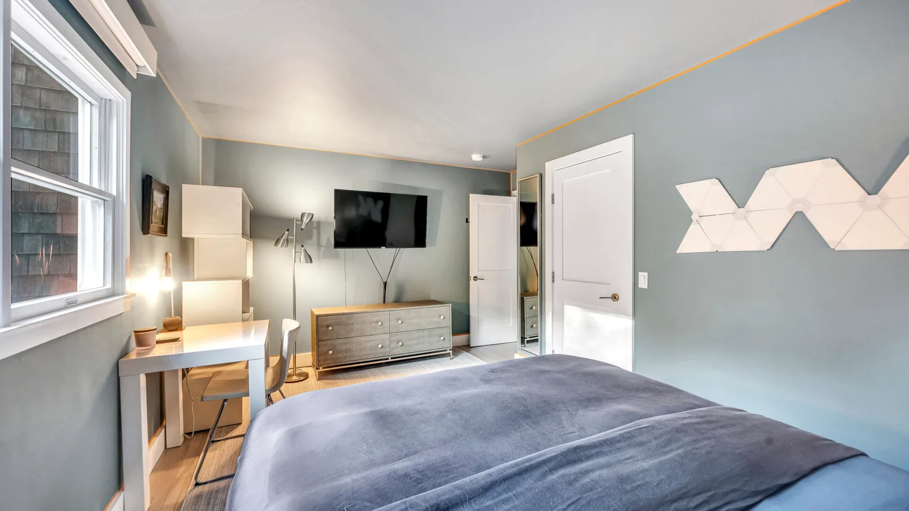 Un dormitorio con una cama, un televisor y un escritorio junto a la ventana.