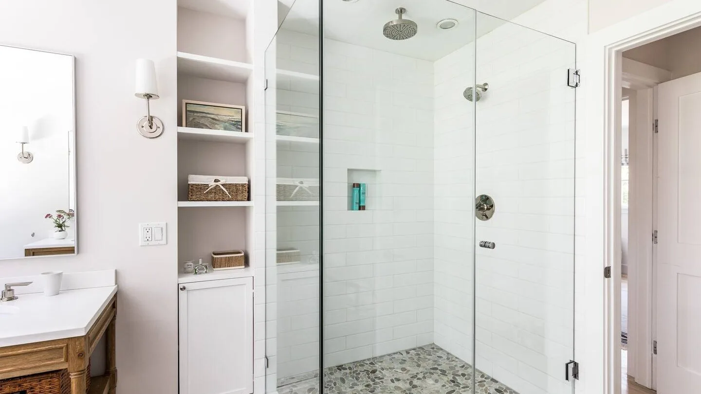 Un baño luminoso con ducha de vidrio y estanterías empotradas.