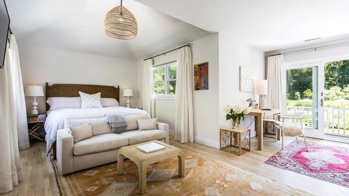 Un dormitorio luminoso con cama, zona de estar y ventanas con vistas a la vegetación.