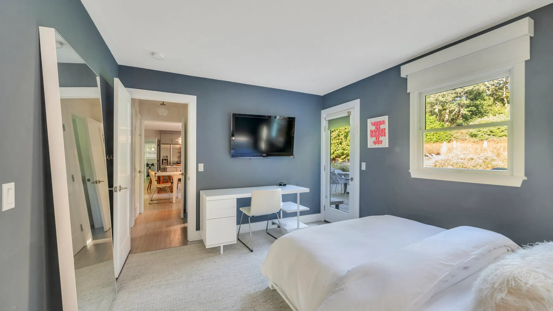 Un dormitorio con cama, escritorio y televisor montado en la pared.