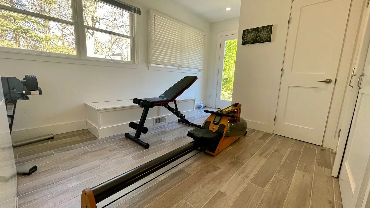 Una sala de ejercicio luminosa con equipo de entrenamiento junto a grandes ventanas.