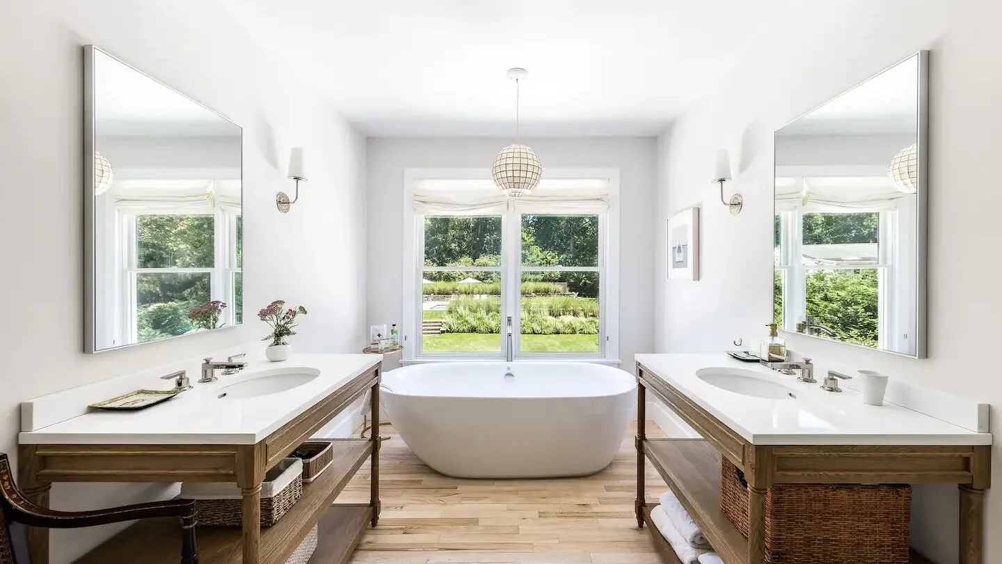 Un baño luminoso tiene una bañera exenta entre dos tocadores con lavabos.