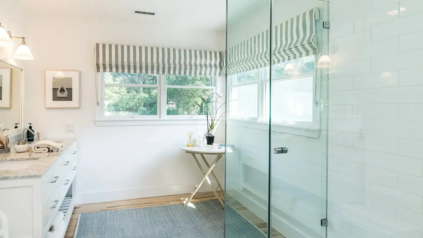 Un baño luminoso con una ducha de vidrio y una ventana con vista a la vegetación.