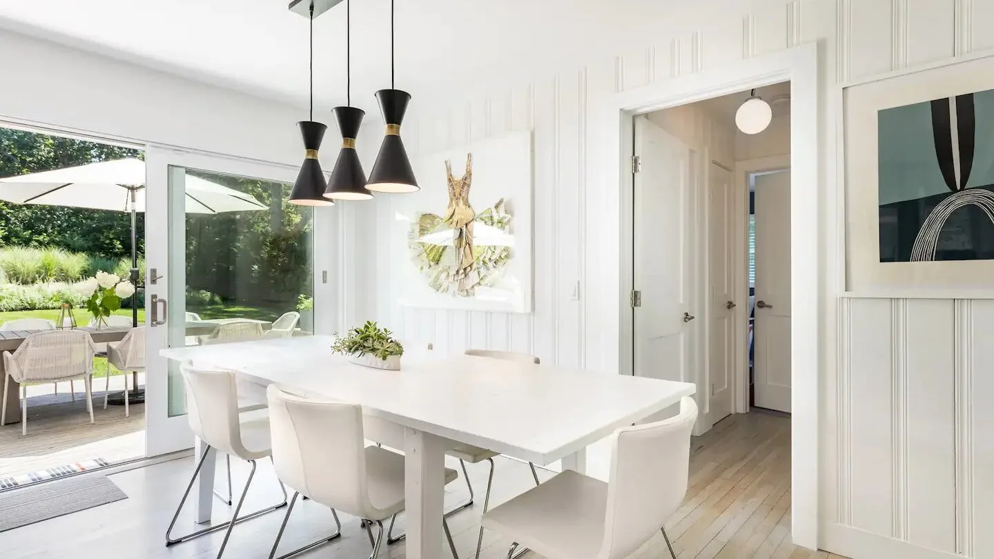 Un comedor luminoso con una mesa blanca y sillas junto a puertas de vidrio abiertas.