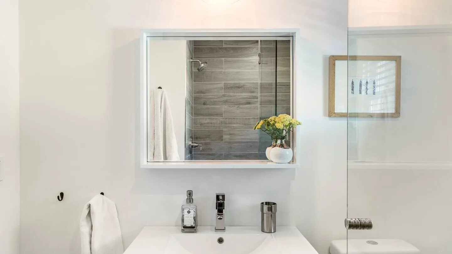Un baño luminoso con un espejo sobre el lavabo y una ducha a la vista.