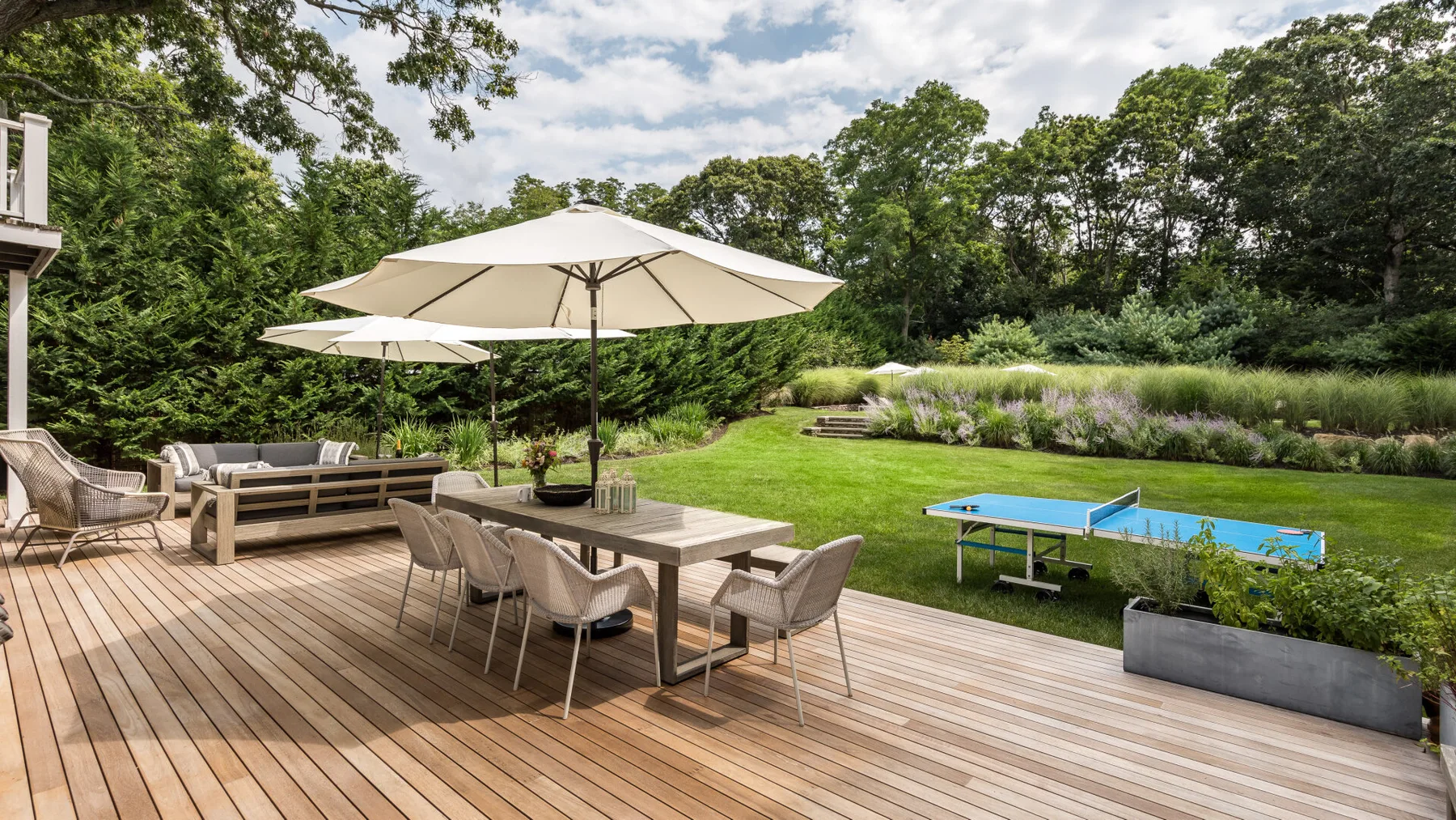 Una amplia terraza exterior tiene asientos para comer, sombrillas y un jardín con una mesa de ping-pong.