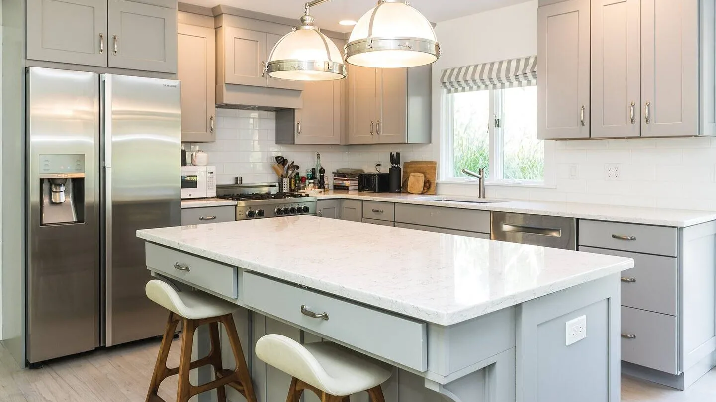 Una cocina luminosa con una isla grande, electrodomésticos de acero inoxidable y lámparas colgantes.