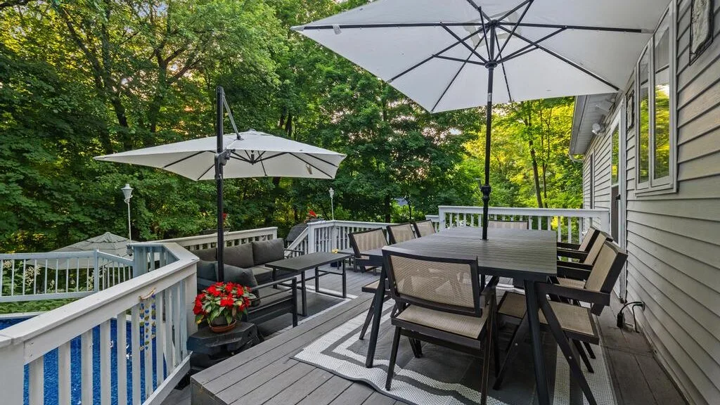 An outdoor deck has a dining table and seating beneath large umbrellas.
