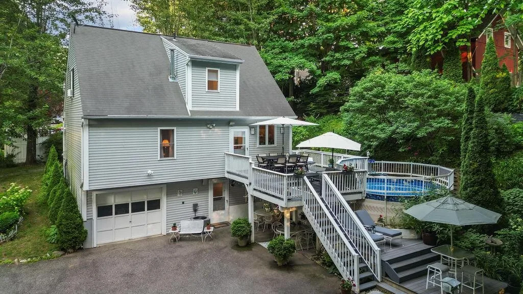 A house with a raised deck and outdoor seating beside a swimming pool.