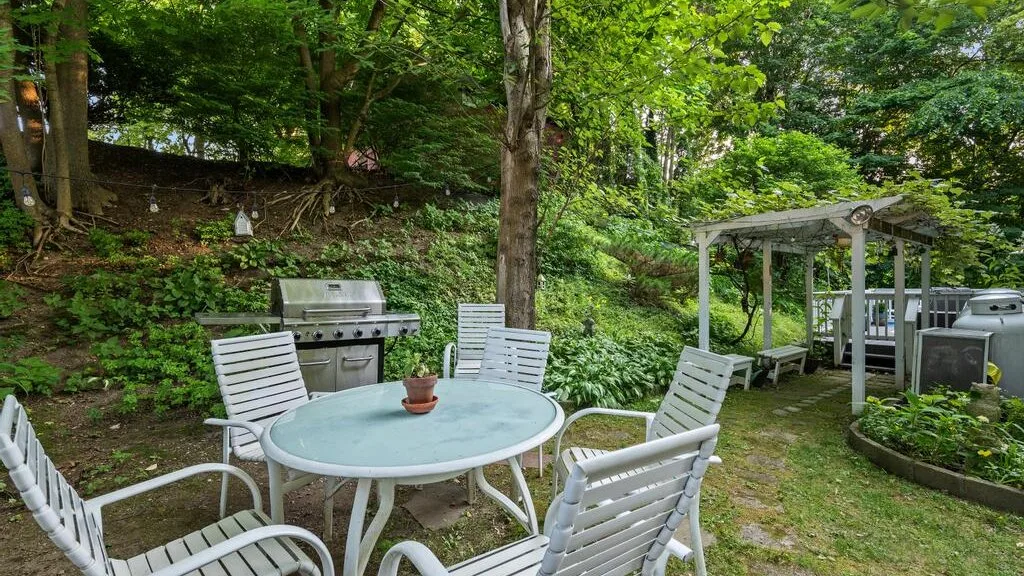 An outdoor dining area with white seating, a grill, and a wooden pergola.