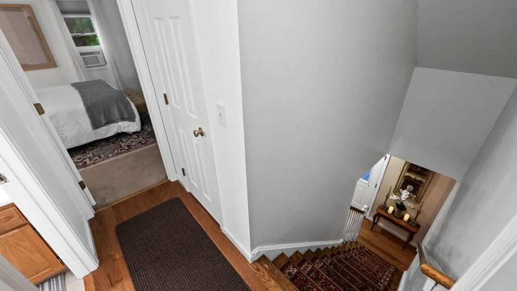 A hallway with a patterned rug leads to a bedroom and a small seating area.