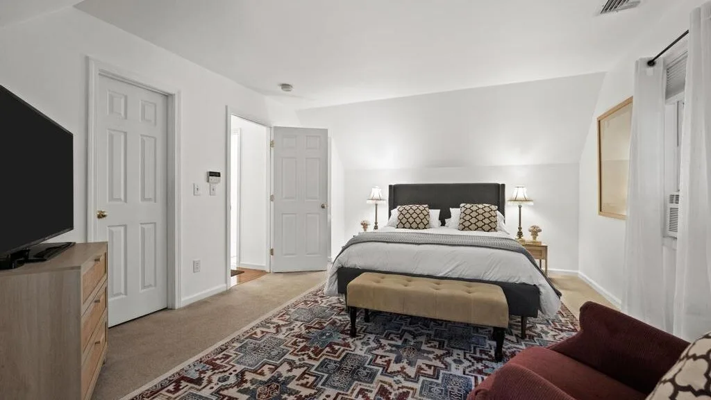 A bedroom with a neatly made bed and a patterned rug.