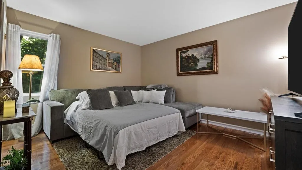 A bedroom with a large bed, gray seating, and framed artwork on the walls.