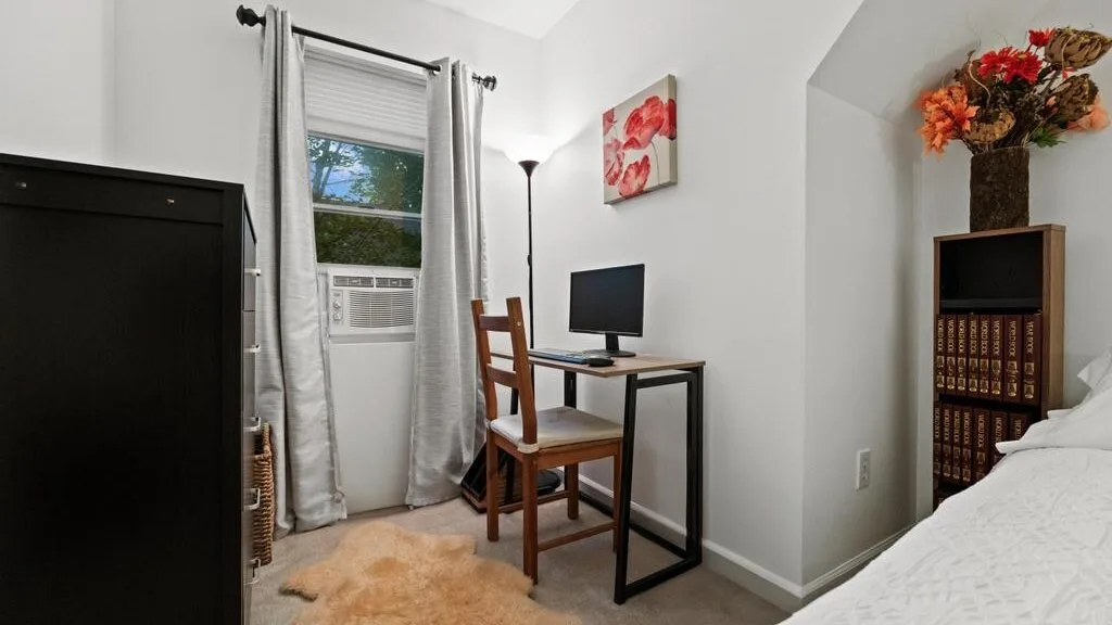 A bedroom with a desk and chair beside a window air conditioner.