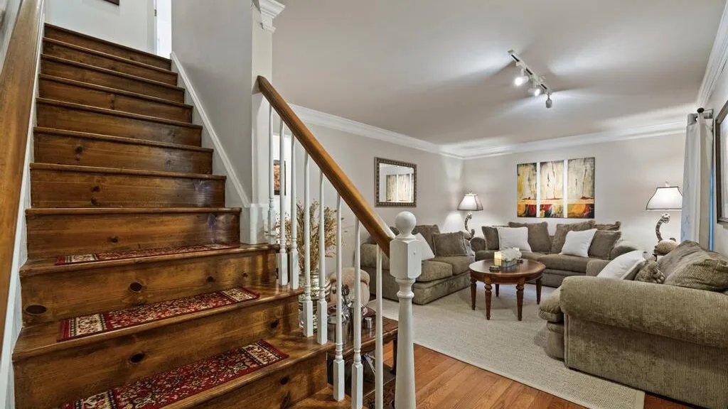 A living room with seating arranged around a coffee table beside a wooden staircase.