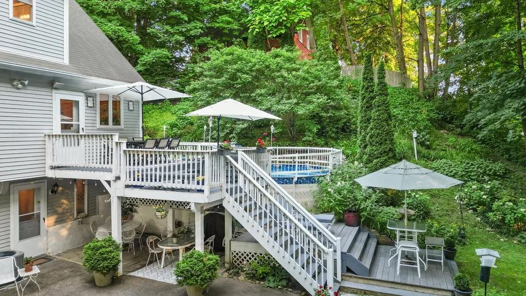 A raised outdoor deck beside a house, with stairs, seating, and surrounding trees.