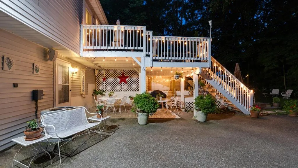 An outdoor patio beside a house, with seating beneath an elevated deck and stairs.