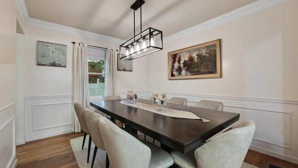 A dining room with a long table, upholstered seating, and a hanging light fixture.