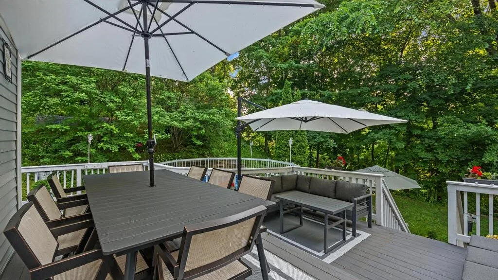 A deck dining area has a table and seating beneath large umbrellas.