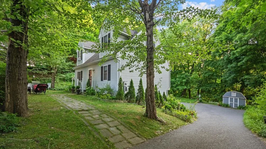 A white house stands among leafy trees beside a paved driveway.