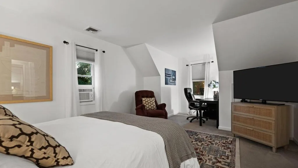A bedroom with a bed, desk, and television beneath a sloped ceiling.