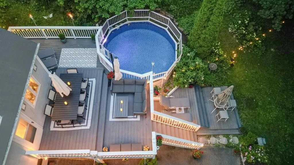 An elevated deck surrounds a round above-ground pool, with outdoor seating nearby.