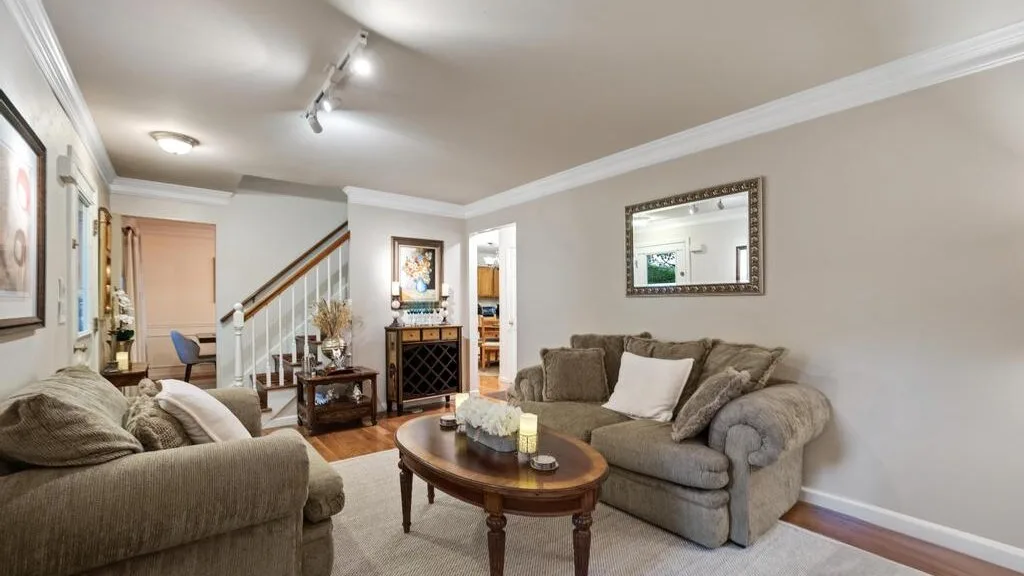 A living room with cushioned seating, a coffee table, and a staircase.