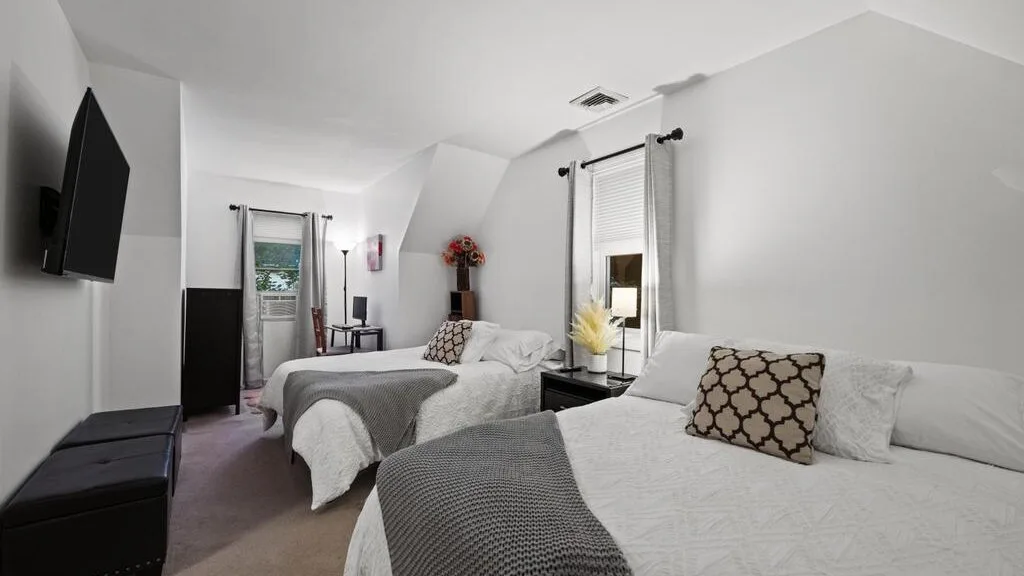 A bright bedroom with two beds and a television mounted on the wall.