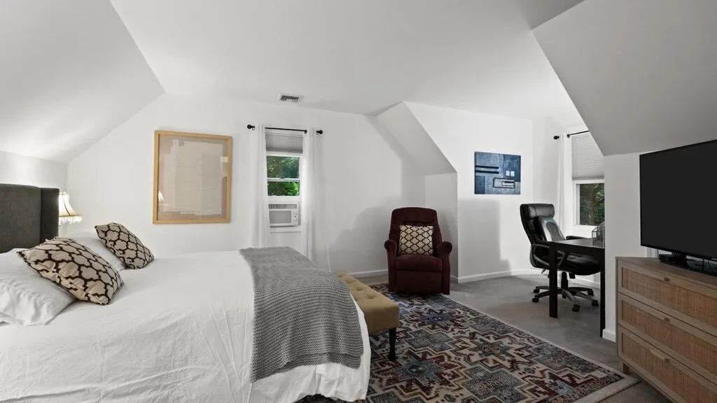 A bedroom with a bed, an armchair, and a desk beneath a sloped ceiling.
