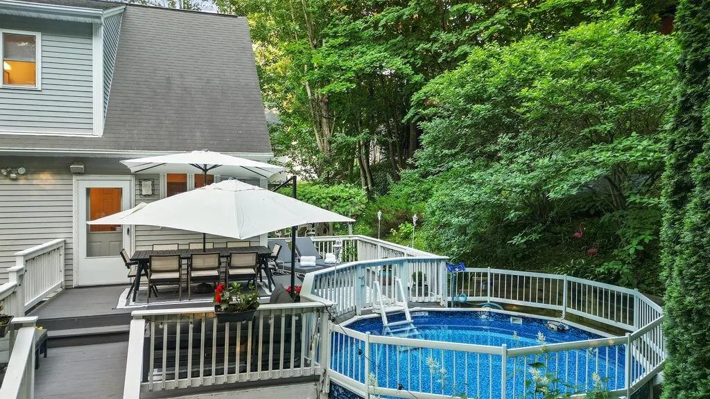 A backyard deck with outdoor seating, a white umbrella, and a fenced pool.