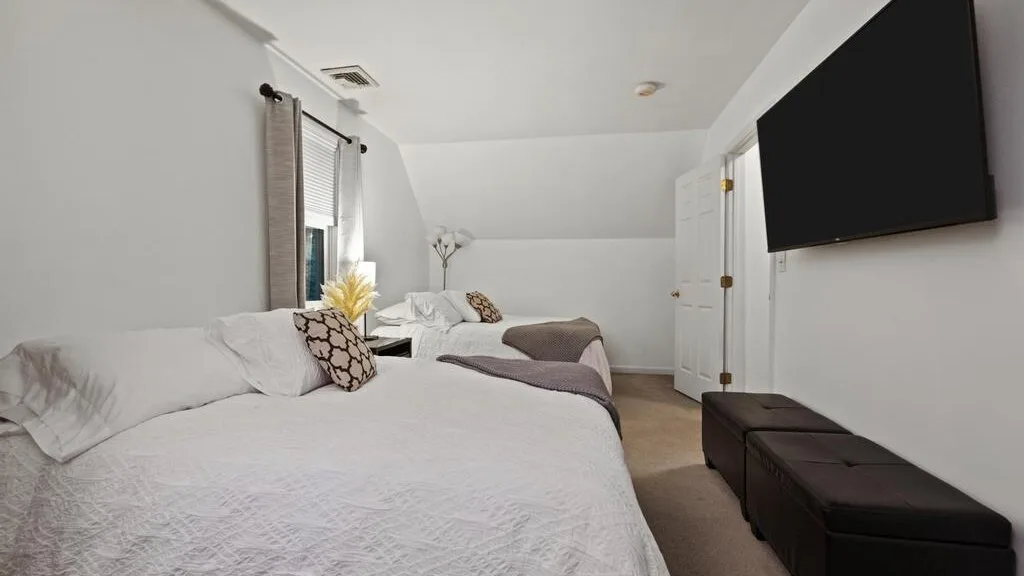 A bedroom with beds beneath a sloped ceiling and a wall-mounted television.