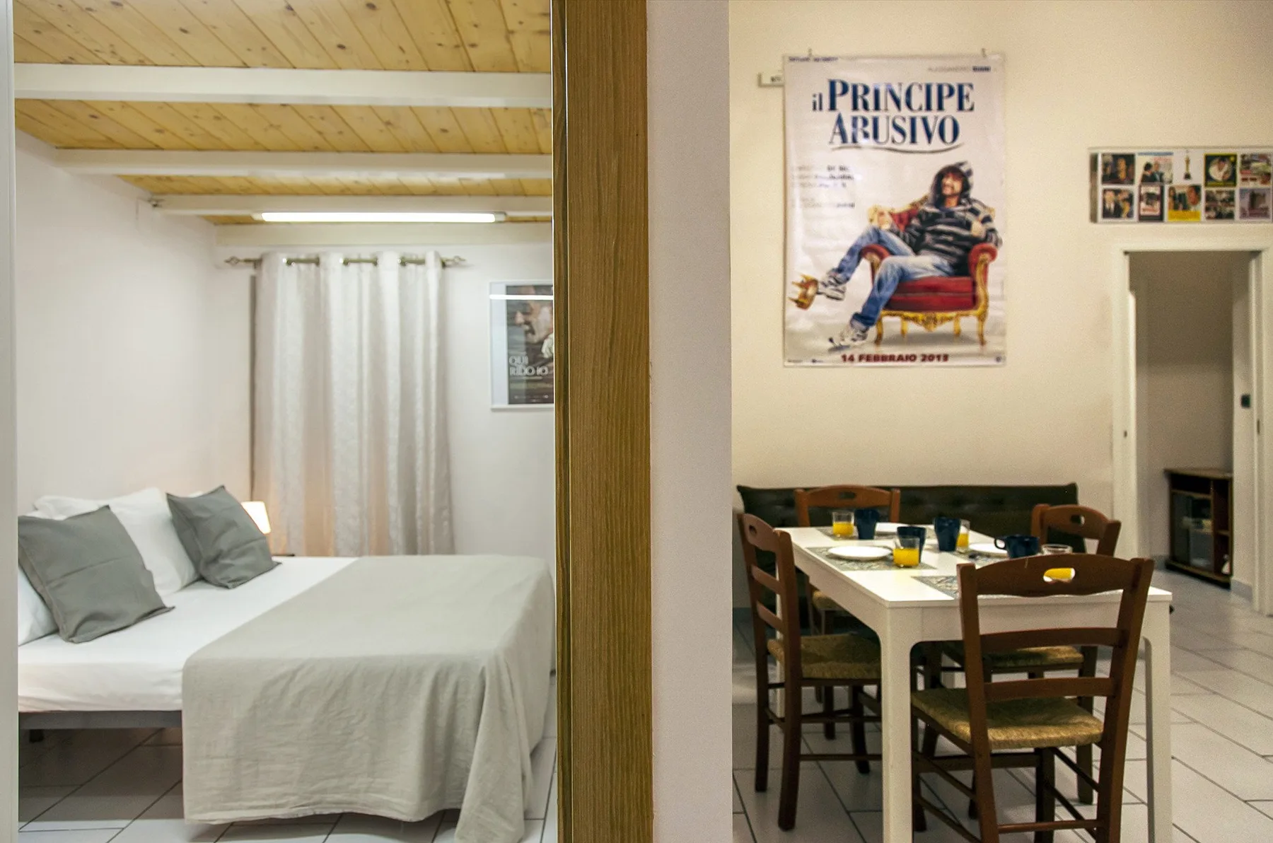 A bedroom with a bed and curtains beside a dining area with a table and chairs.