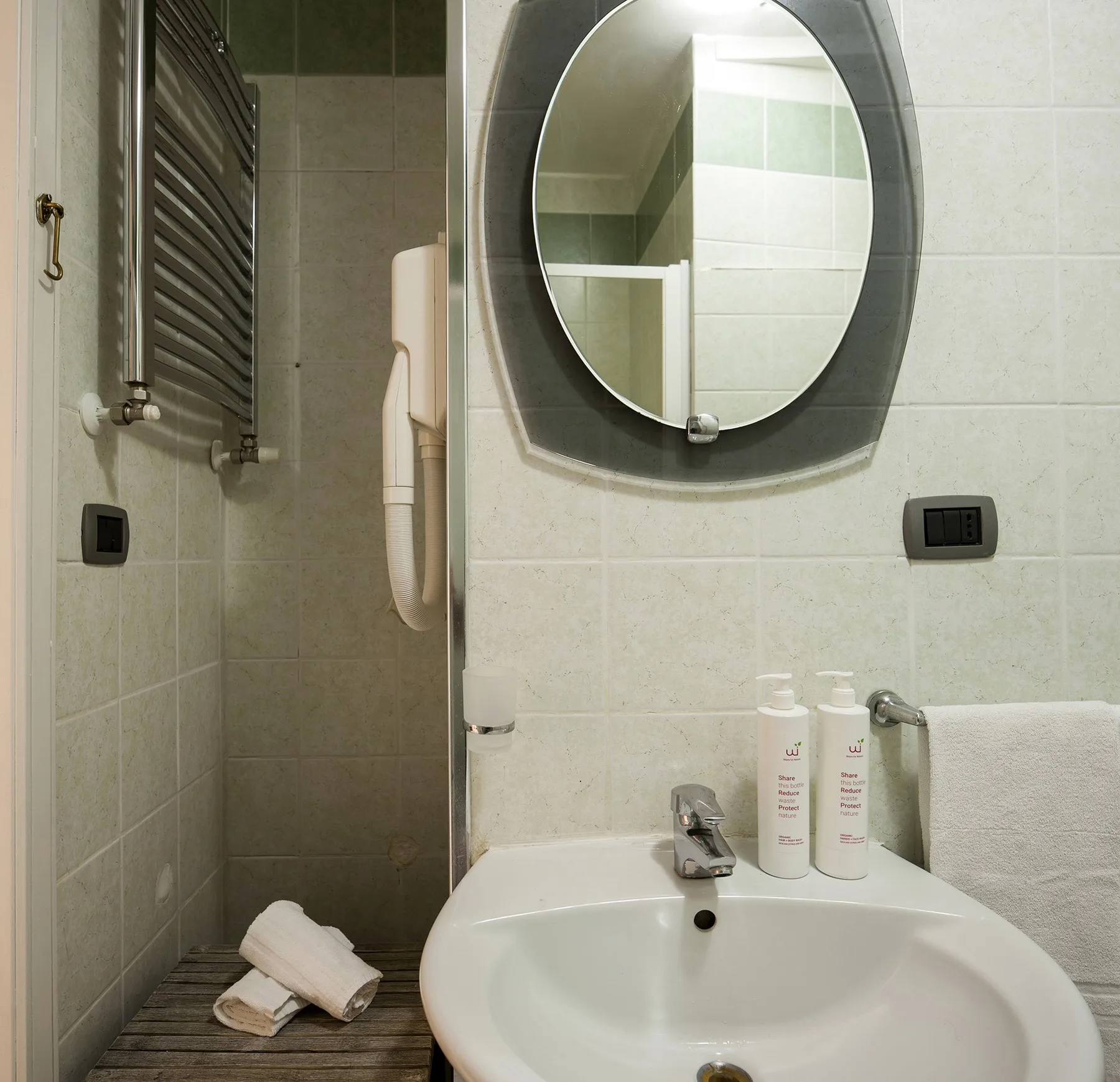 A tiled bathroom with a sink, round mirror, and folded towels.