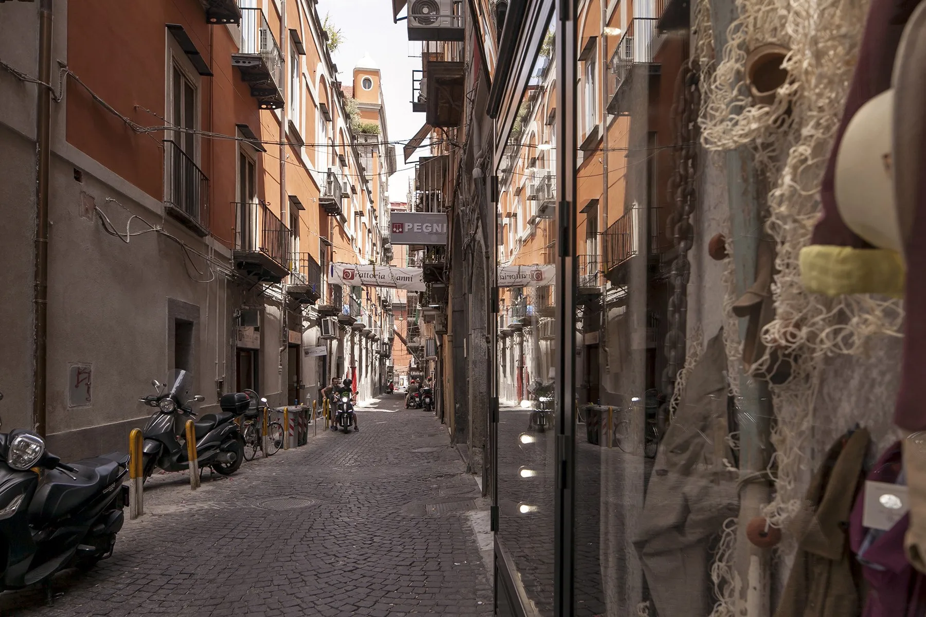 A narrow cobblestone street runs between closely spaced buildings and storefronts.