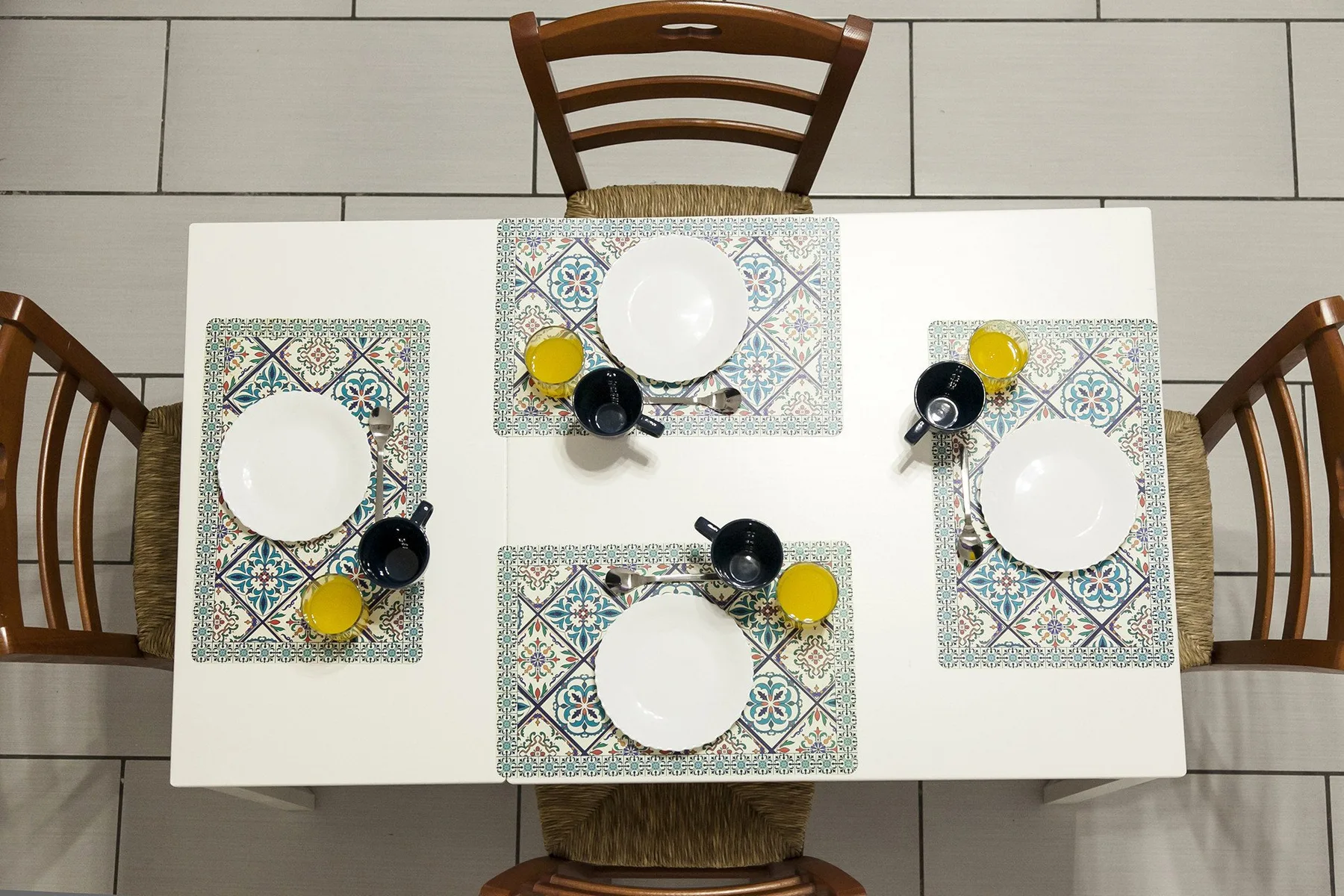 A dining table is set with plates, colorful placemats, and dark cups.