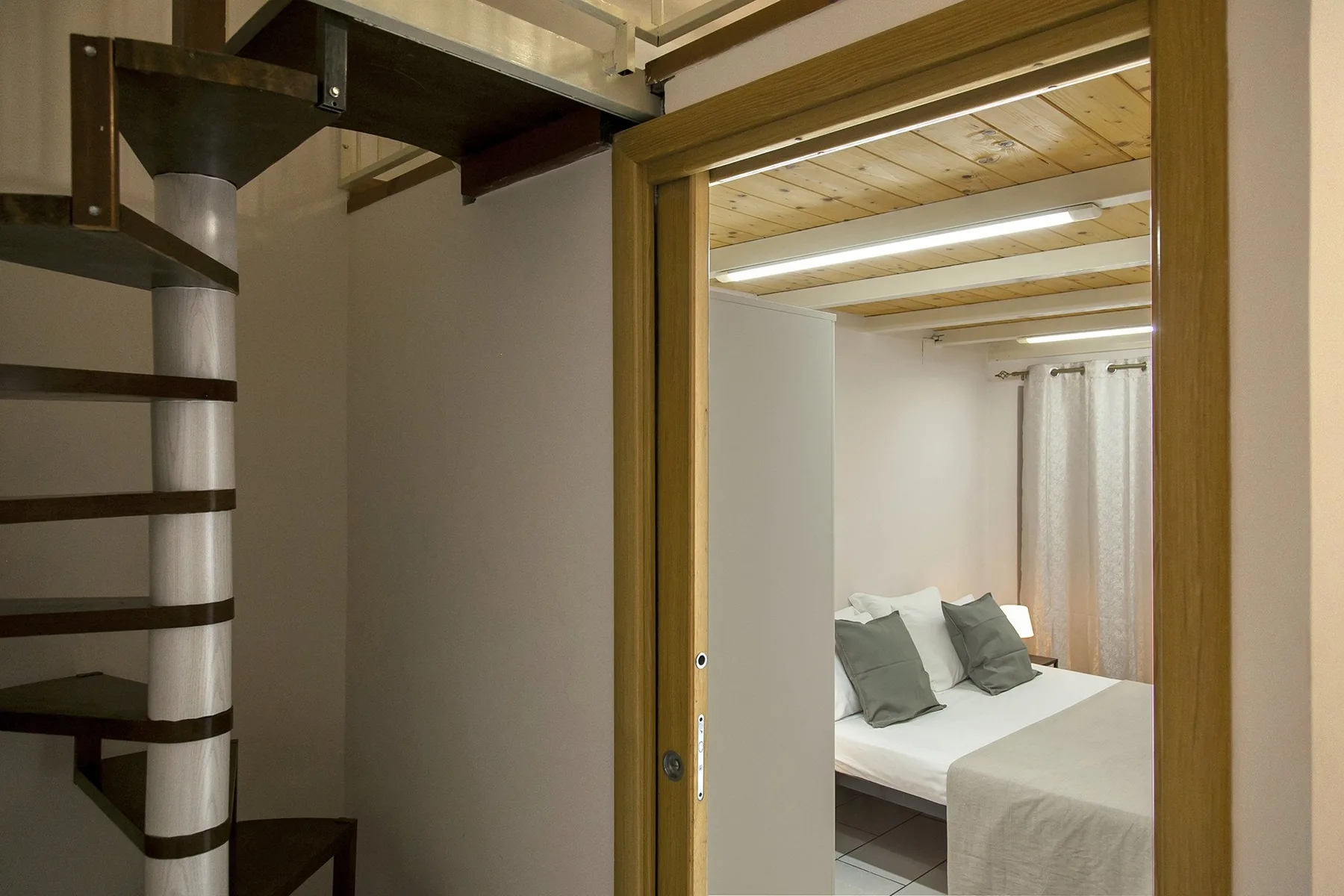 A bedroom with a neatly made bed and light curtains.