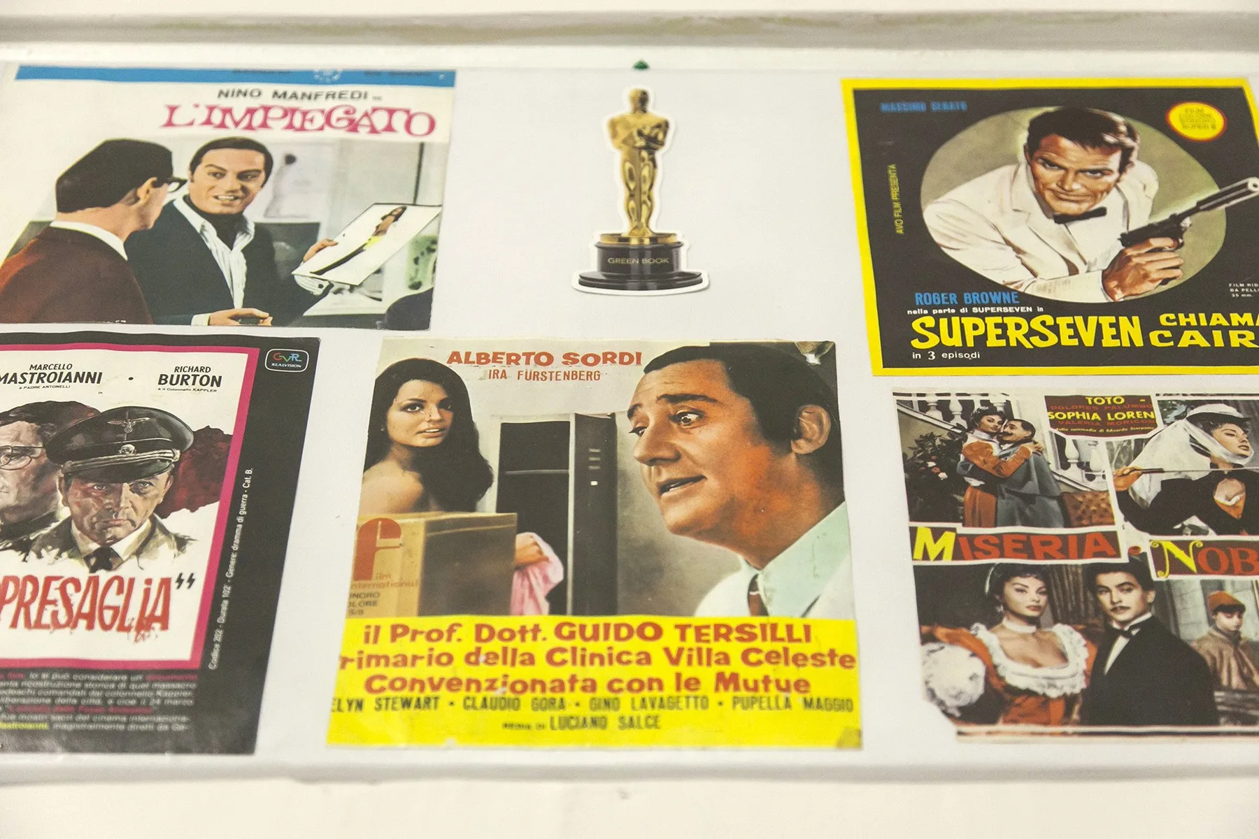 A display of vintage Italian film posters surrounds a small gold-colored statuette.