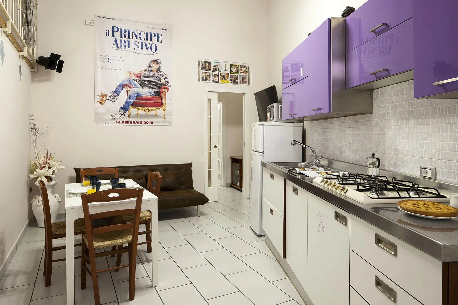A kitchen and dining area with purple cabinets and a table beside a sofa.