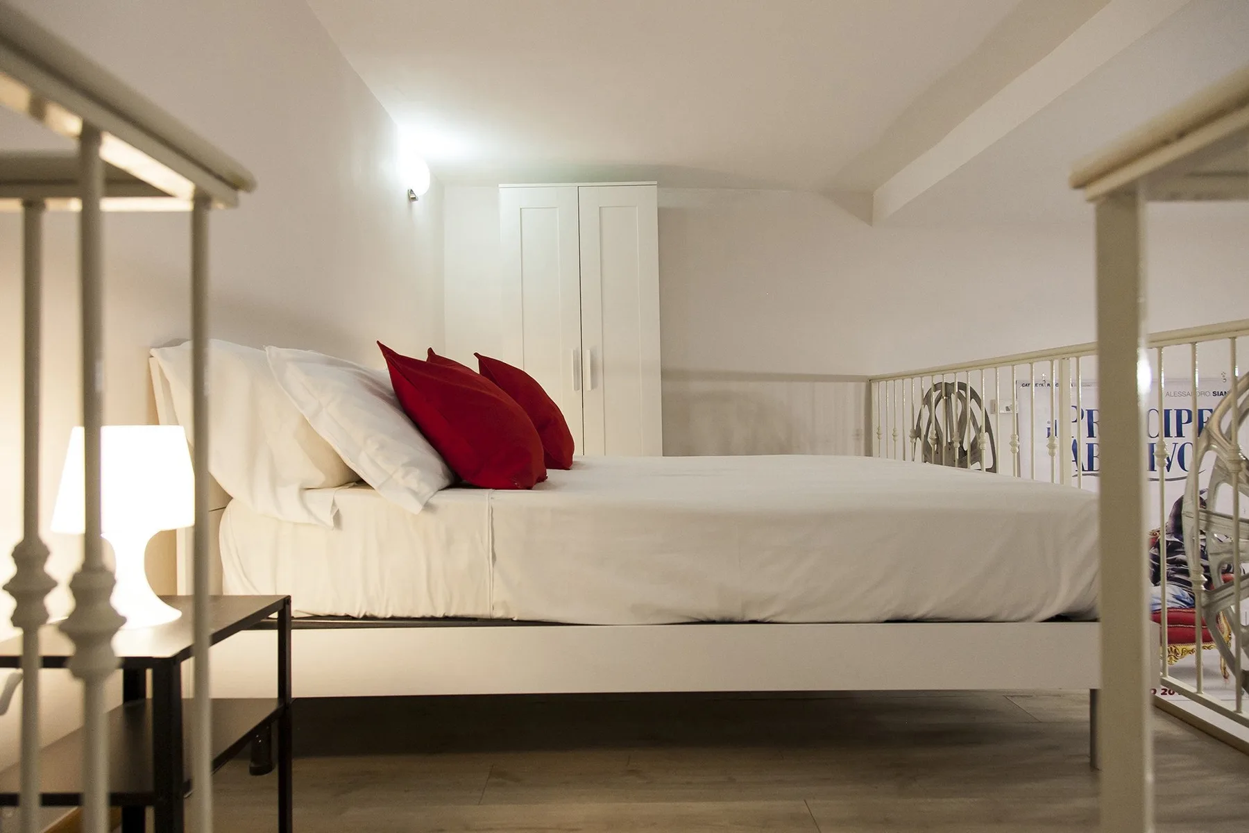 A bedroom with a raised bed, white bedding, and red accent pillows.