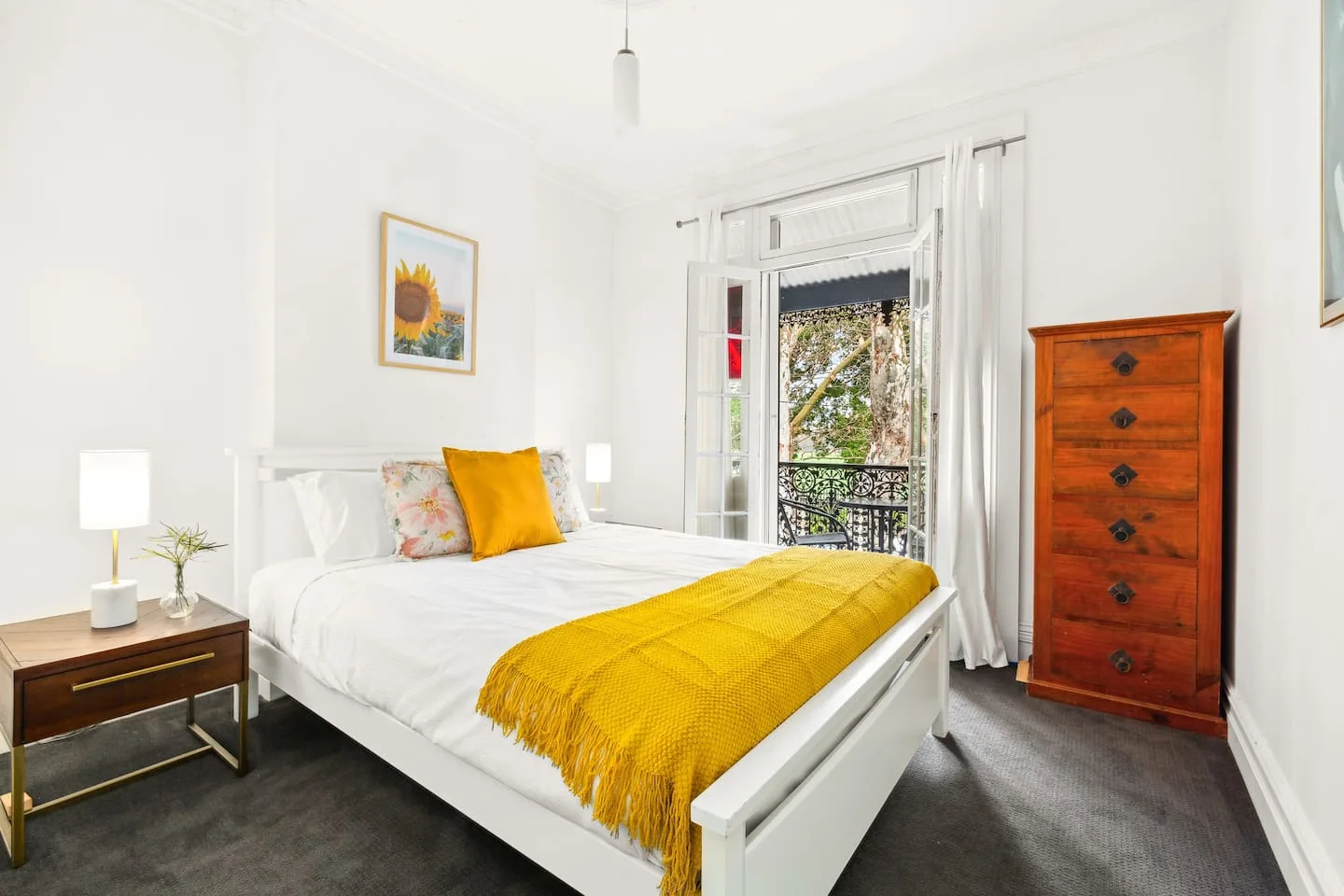 Un dormitorio luminoso con una cama blanca y la puerta del balcón abierta.