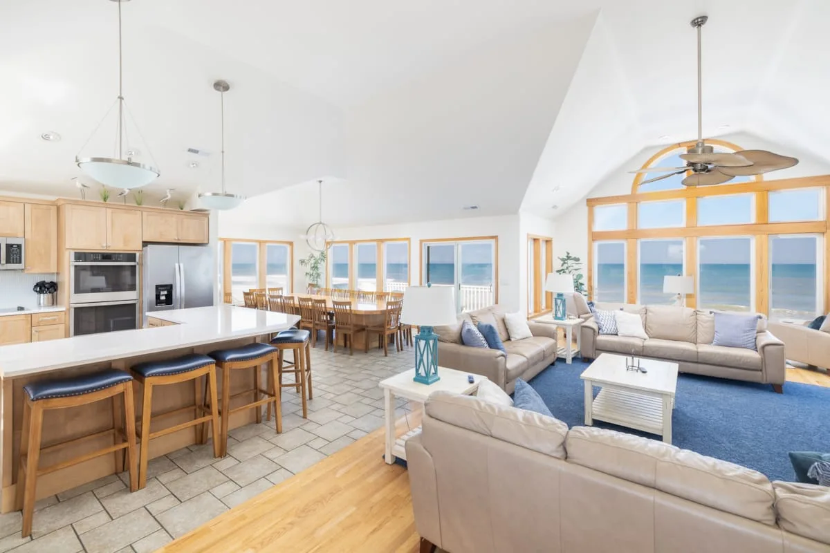 Open-plan living room and kitchen with seating beside large windows overlooking the ocean.