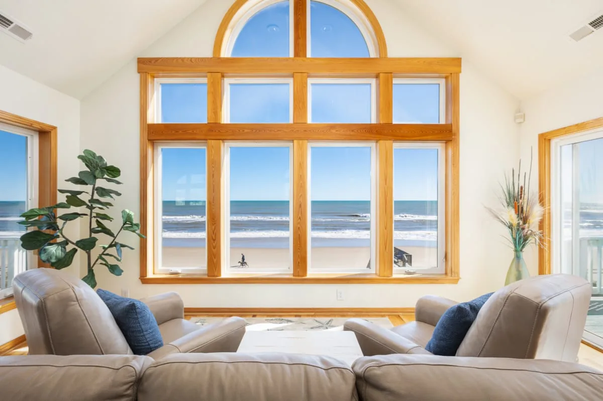 A bright living room with seating facing large windows overlooking the beach.