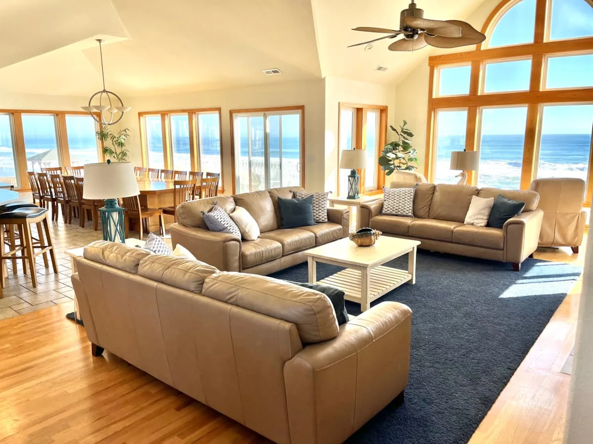 A bright living and dining area has seating around a coffee table and ocean views.