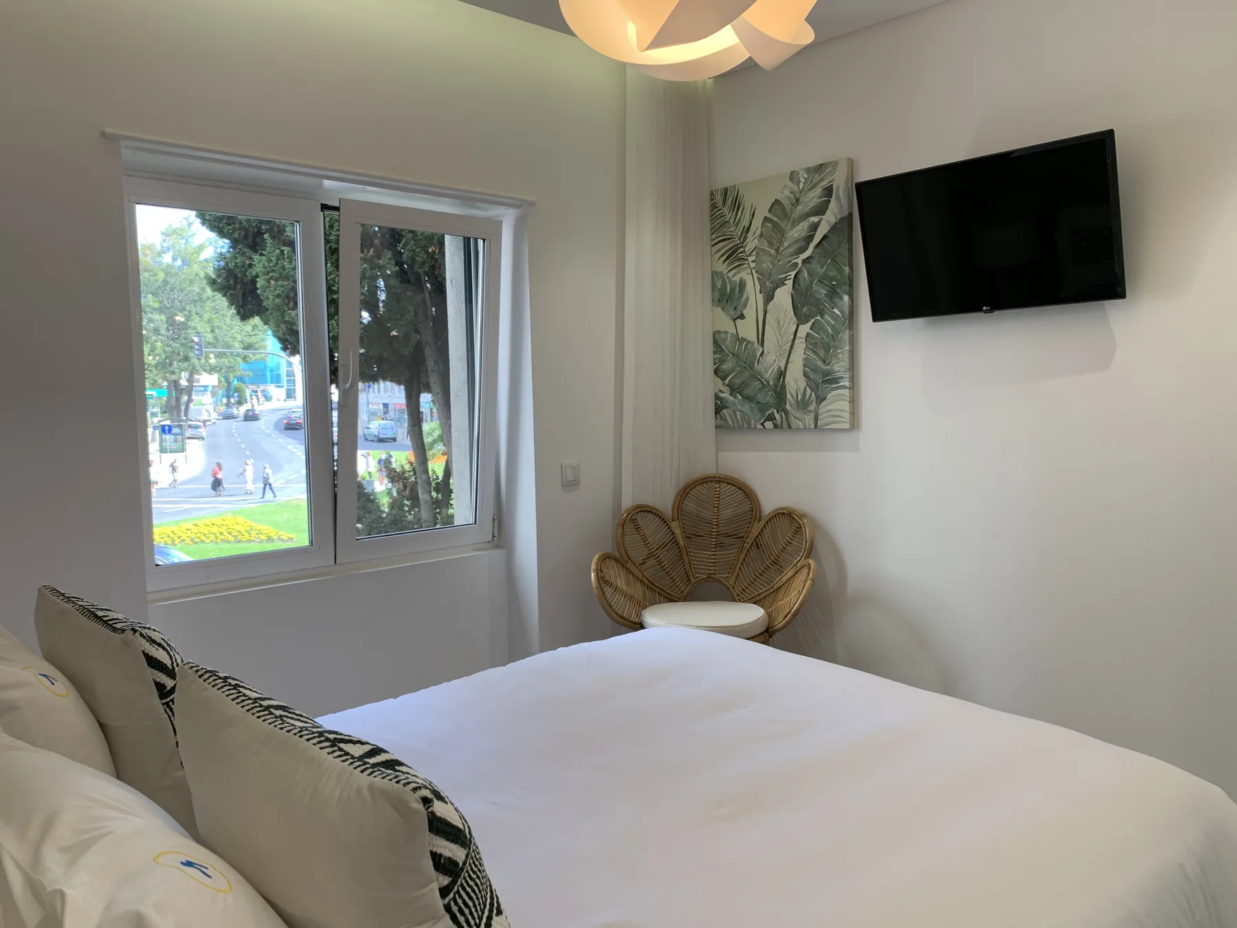 Un dormitorio con una cama, un televisor en la pared y una ventana con vistas a la calle.