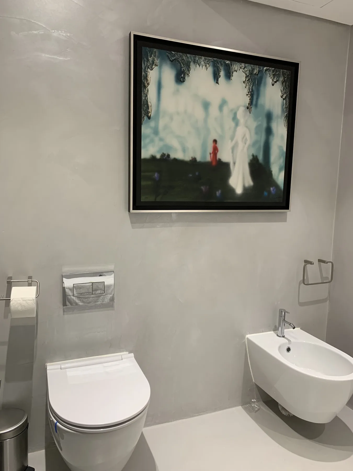 Un baño moderno con un lavabo suspendido y una obra enmarcada sobre el inodoro.