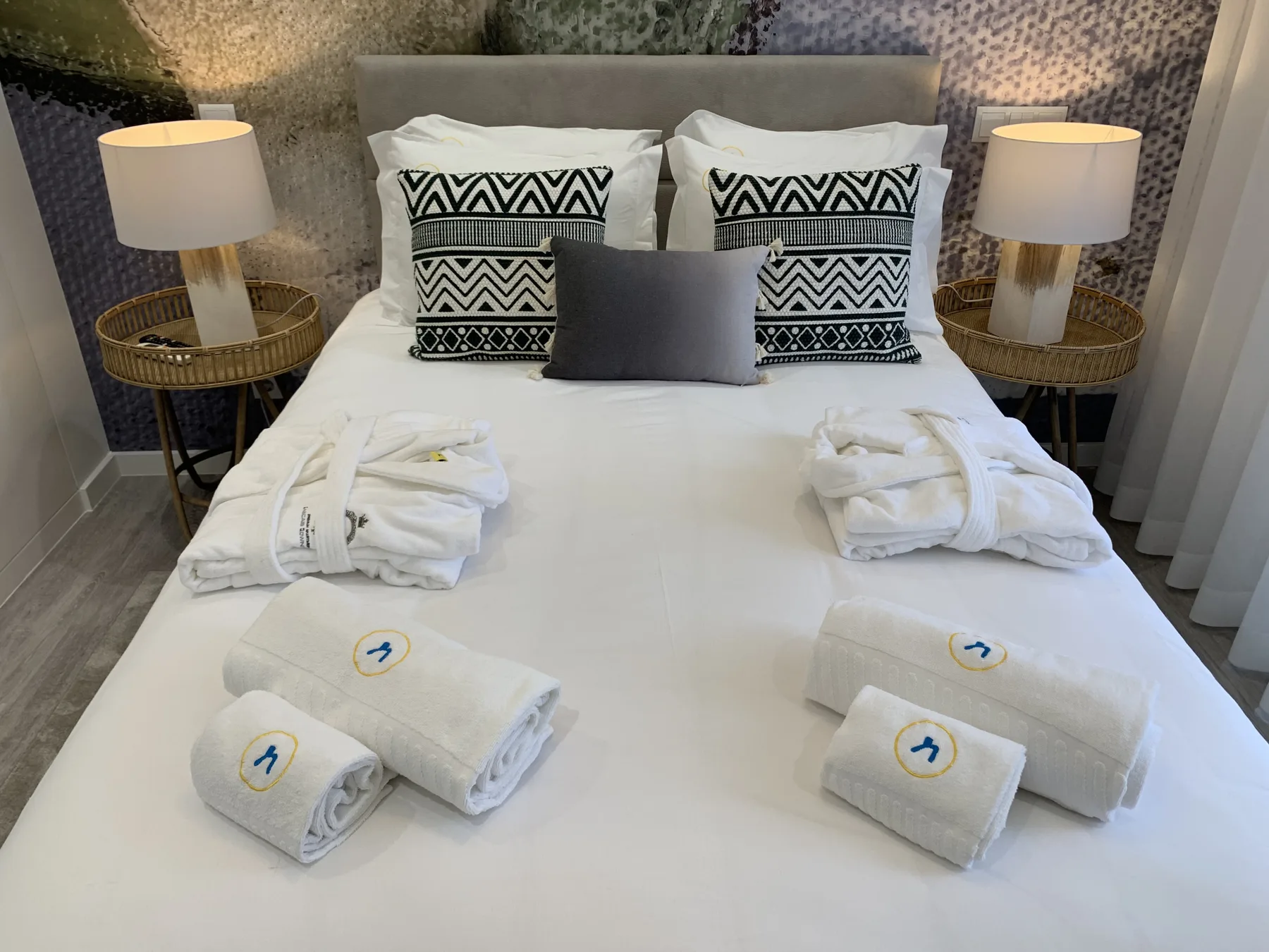 Un dormitorio con la cama hecha, cojines estampados y toallas dobladas.