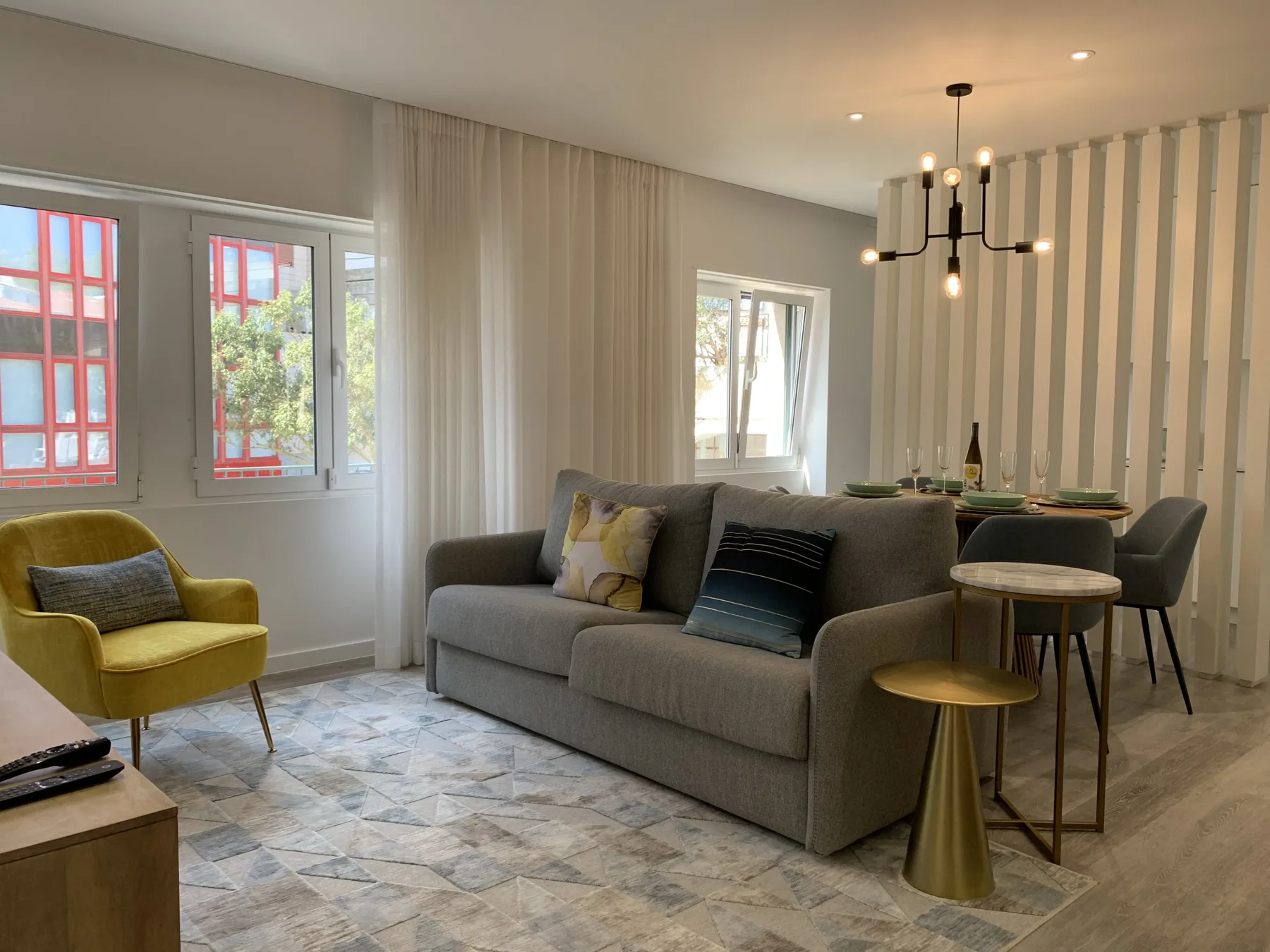 Una sala de estar y comedor con un sofá gris, una mesa y ventanas altas.